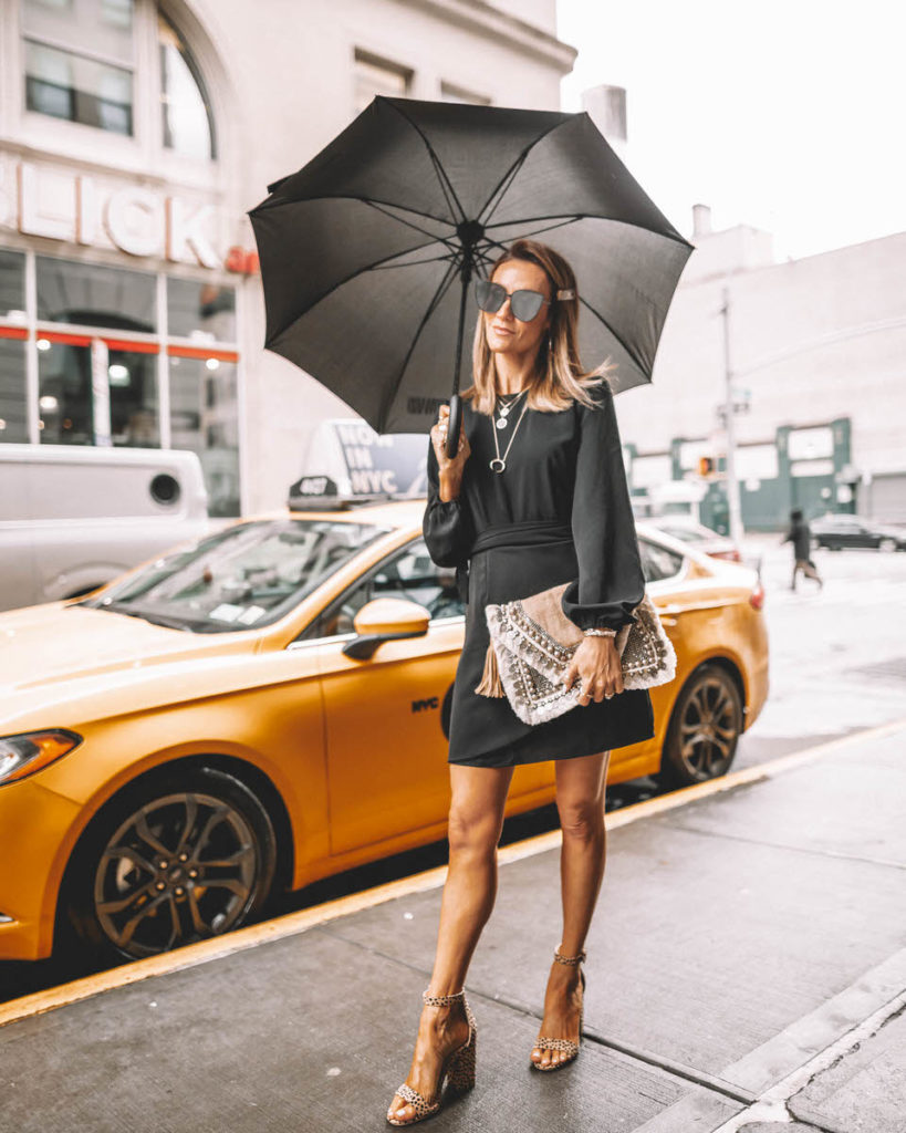 Fashion Blogger Karina Reske in a Vici Black Dress | embellished clutch | leopard print slides | holding an umbrella | street style | NYFW NYFW outfits and tips featured by top US fashion blogger, Karina Style Diaries: image of a woman wearing an Express black neck dress, ASOS leopard sandals, Shashi clutch and a Gorjana pendant necklace