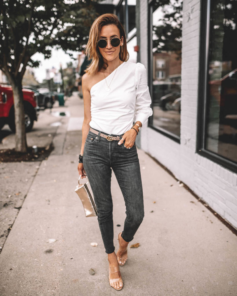 Karina Style Diaries wearing one-shoulder trend Revolve white top Levi's wedgie high waist black jeans clear heels Gucci Belt outfit