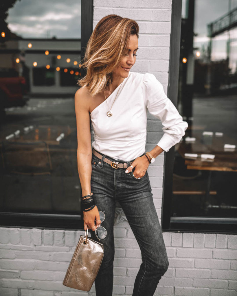 Karina Style Diaries wearing one-shoulder trend Revolve white top Levi's wedgie high waist black jeans clear heels Gucci Belt outfit