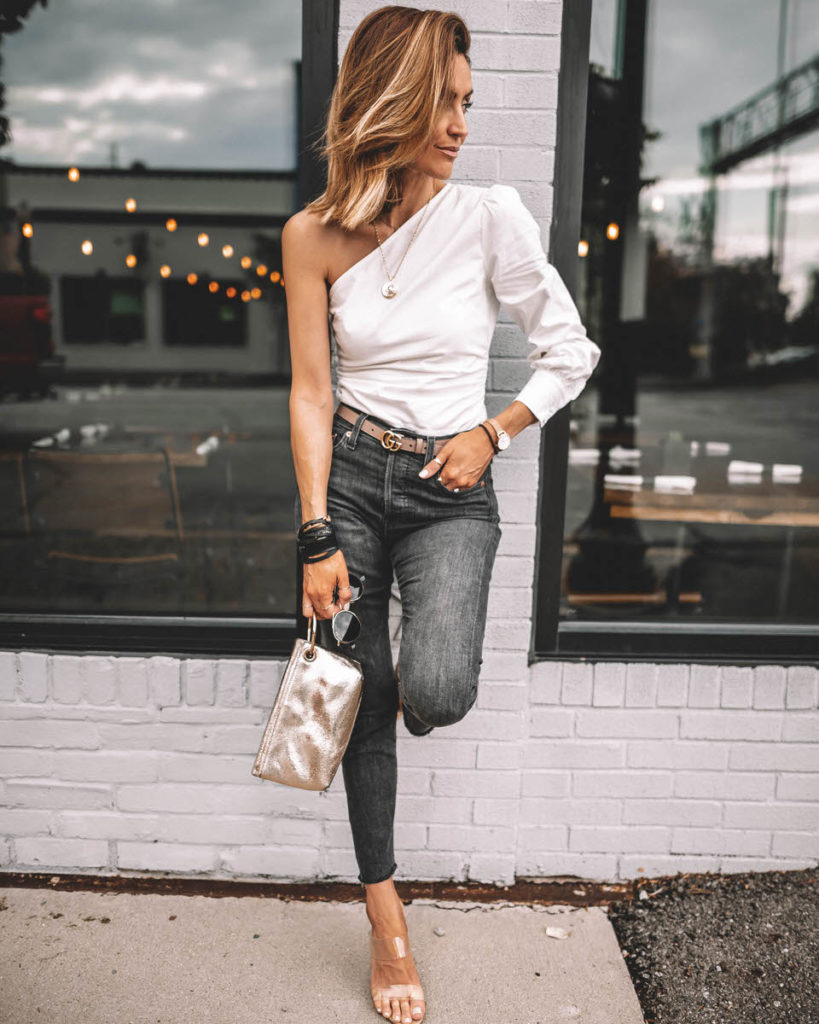 Karina Style Diaries wearing one-shoulder trend Revolve white top Levi's wedgie high waist black jeans clear heels Gucci Belt outfit