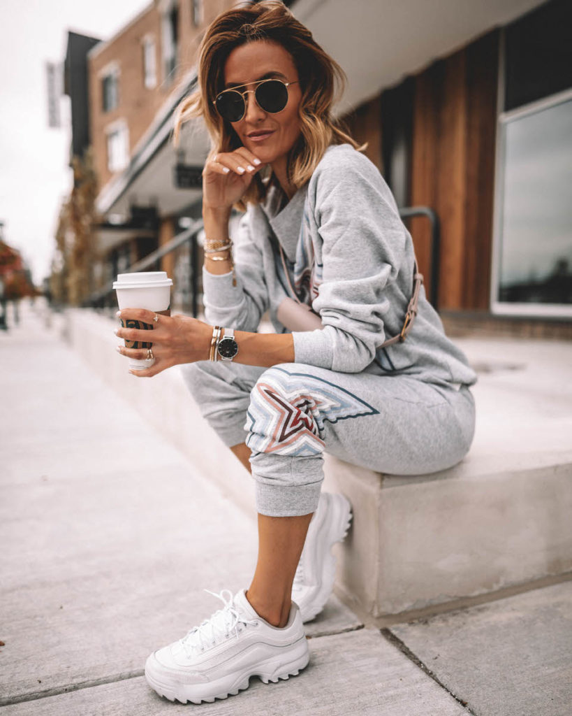 Karina Style Diaries seating having coffee wearing grey star swetshirt pant set  white sneakers pink belt bag across the chest