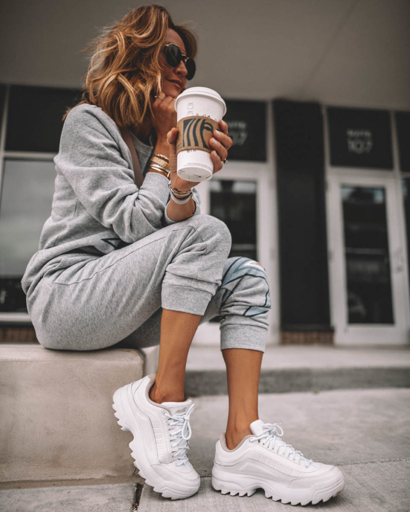 Karina Style Diaries seating having coffee wearing grey star swetshirt pant set white sneakers pink belt bag across the chest