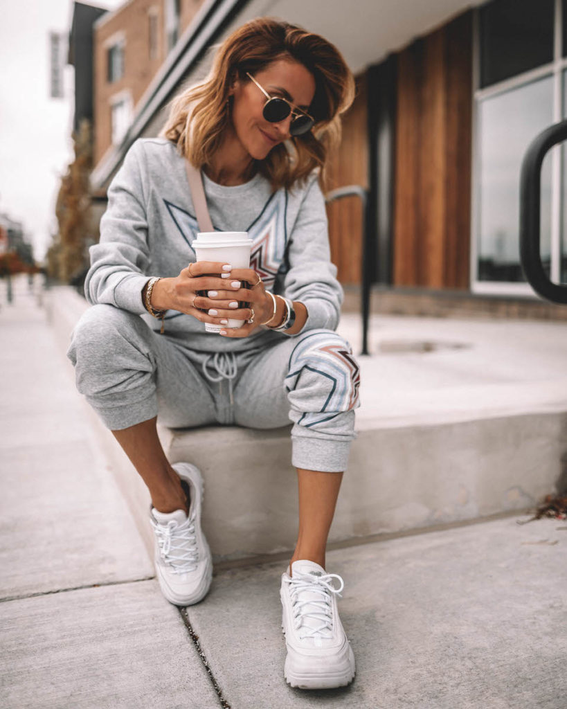 Karina Style Diaries seating having coffee wearing grey star swetshirt pant set white sneakers pink belt bag across the chest