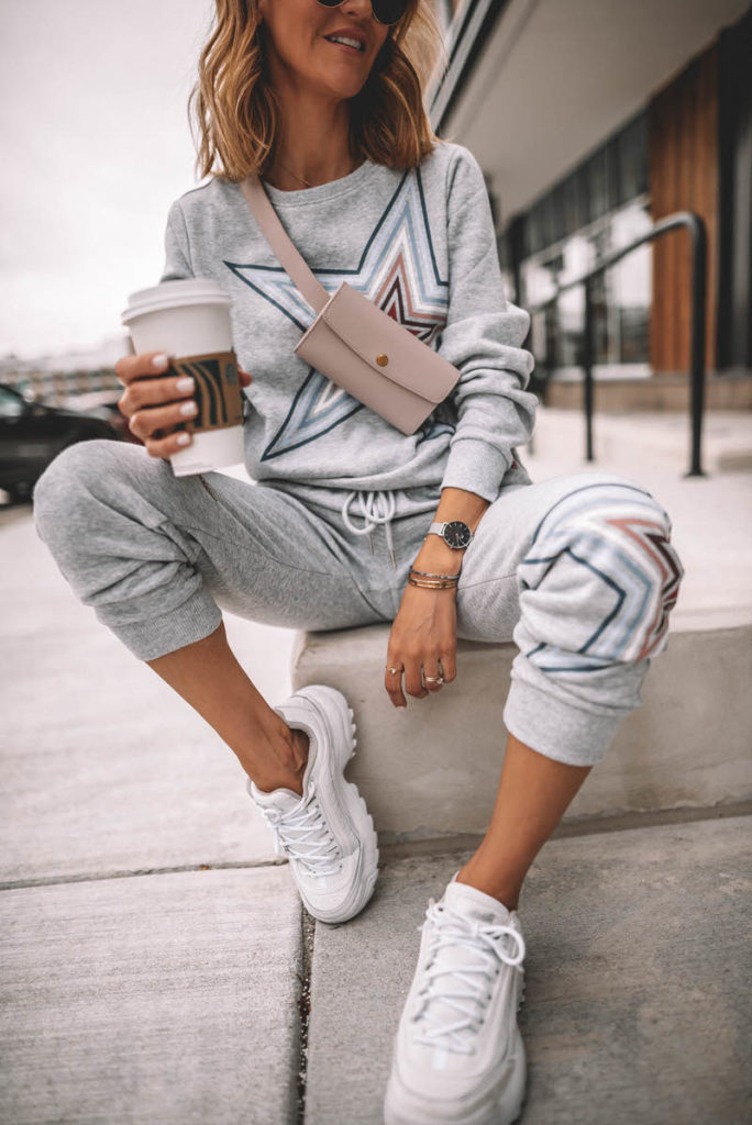 Karina Style Diaries seating having coffee wearing grey star swetshirt pant set white sneakers pink belt bag across the chest