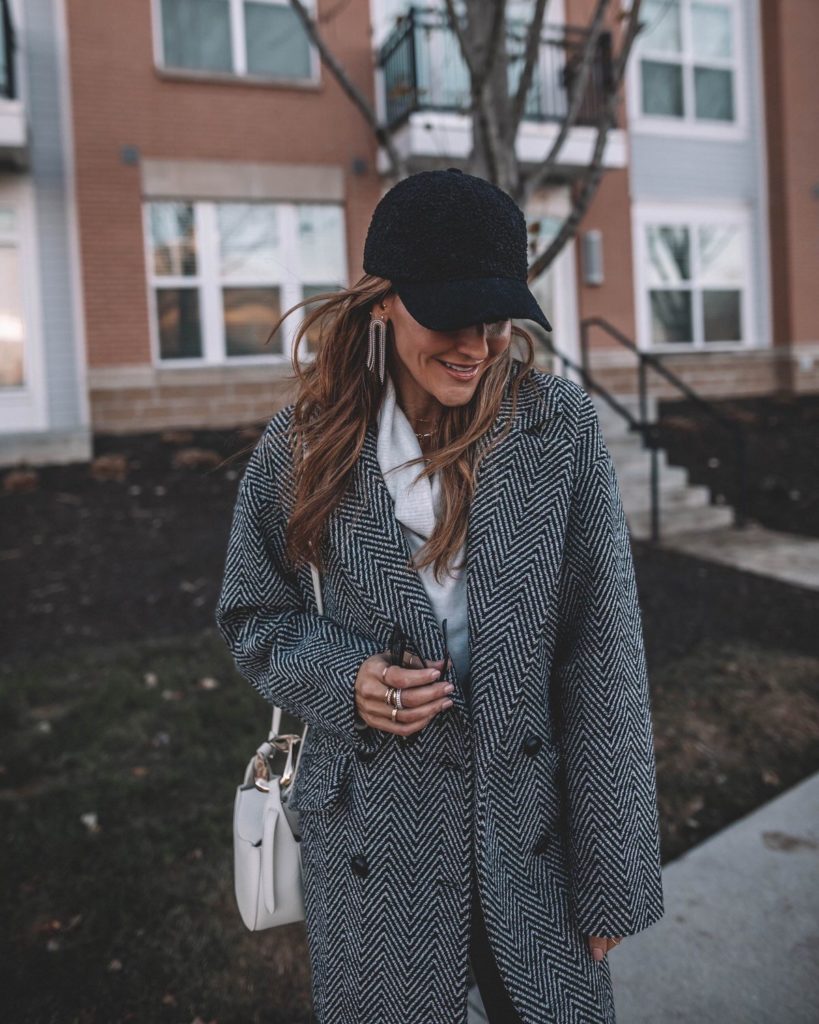 Karina wears black and white wool coat with sherpa ballcap