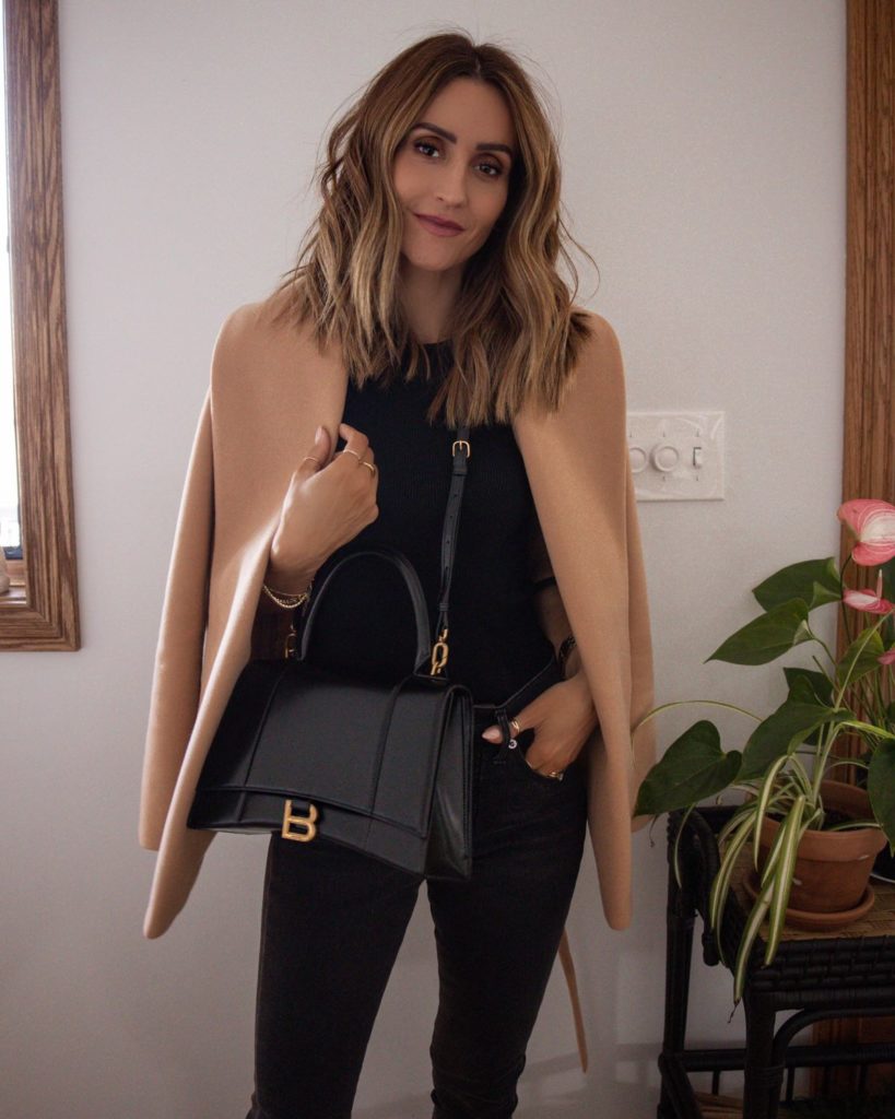 Karina wears express camel wrap coat with black sweater tank and black jeans and balenciaga bag