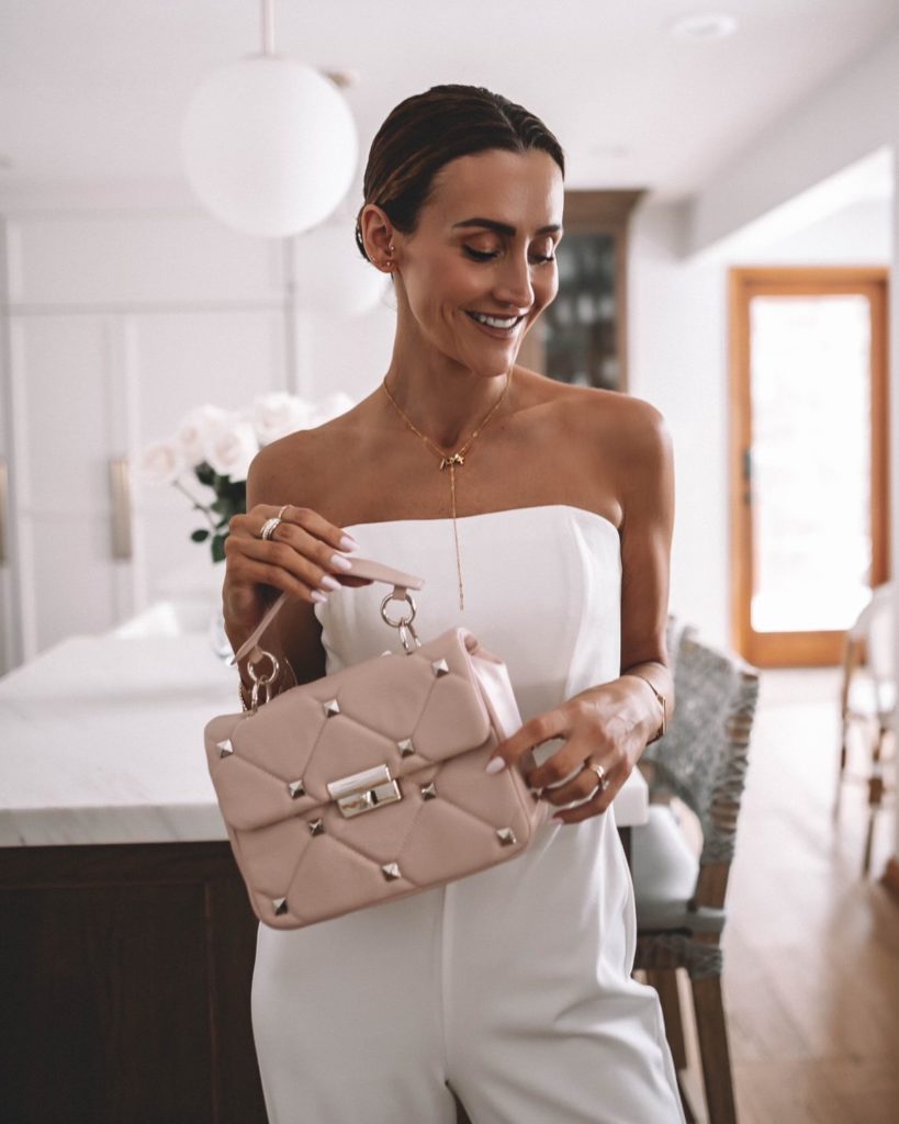 Karina wears white house black market white jumpsuit with pink handbag