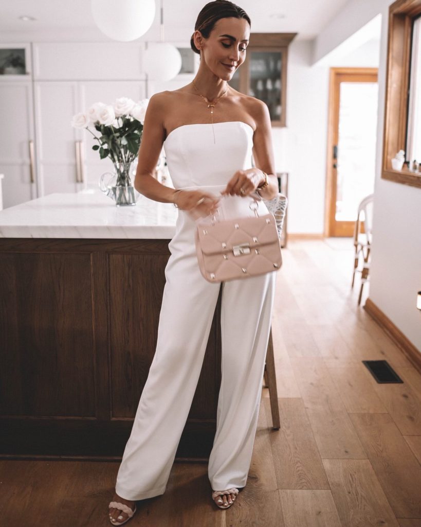 Karina wears white house black market white jumpsuit with pink handbag