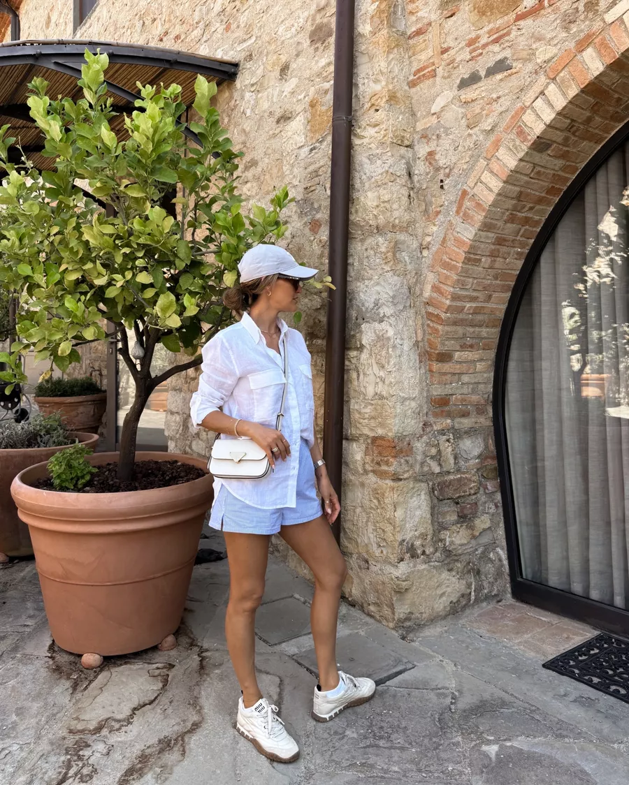 Blue and white stripped boxer shorts, white linen button up shirt, Celine ball cap, Prada crossbody bag, Miu Miu technical sneakers, Quai sunnies 