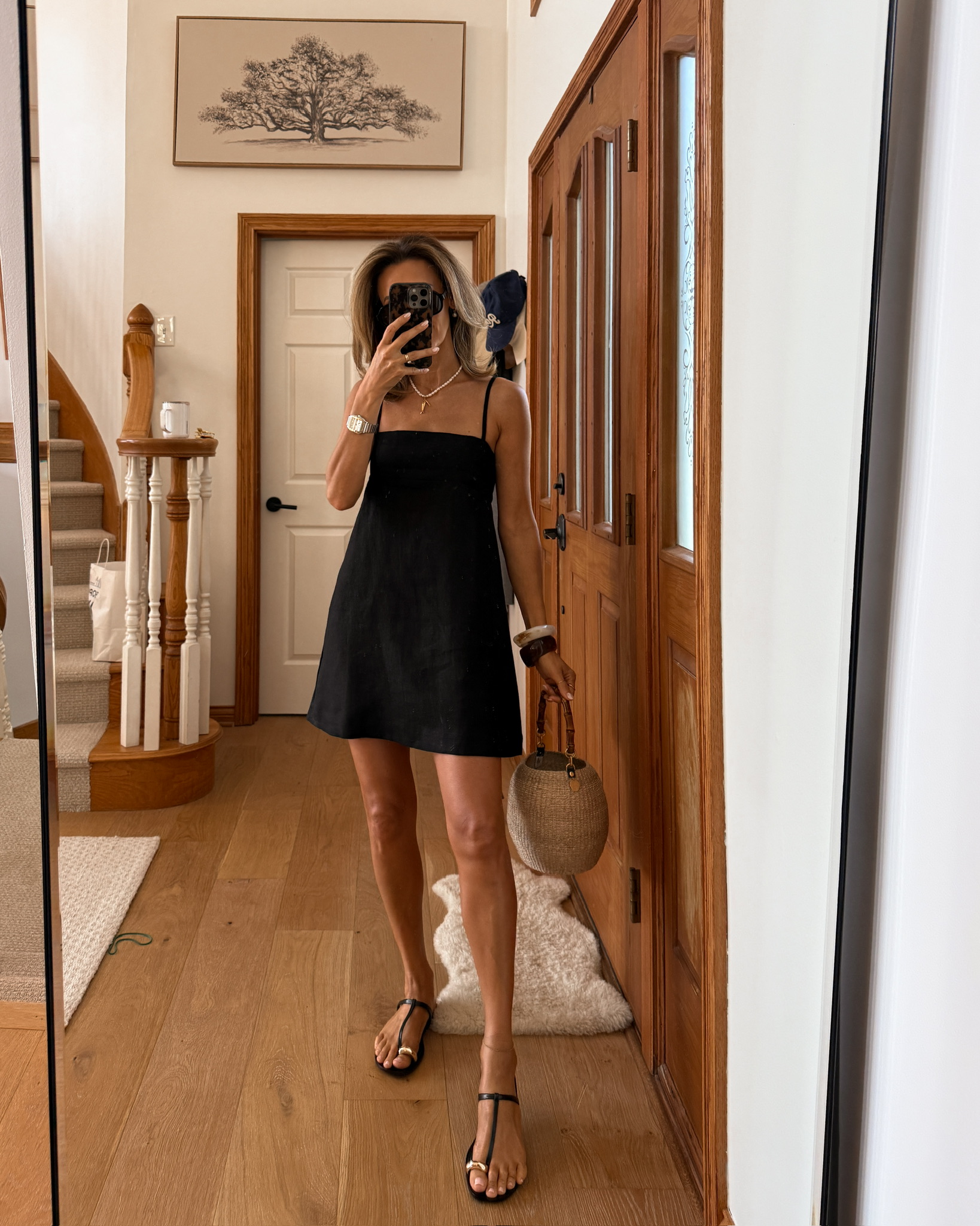 a line black mini linen dress, black sandals with gold details, pearl necklace, woven basket bag, chunky bangles